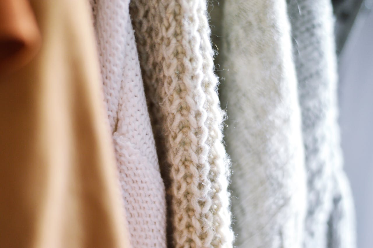 Detailed view of multiple woolen knitted sweaters in soft, neutral colors emphasizing texture and warmth.